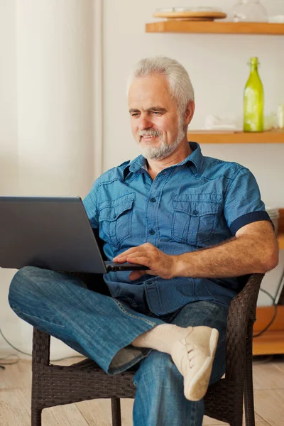 Senior man met laptop zit op de keuken — Stockfoto