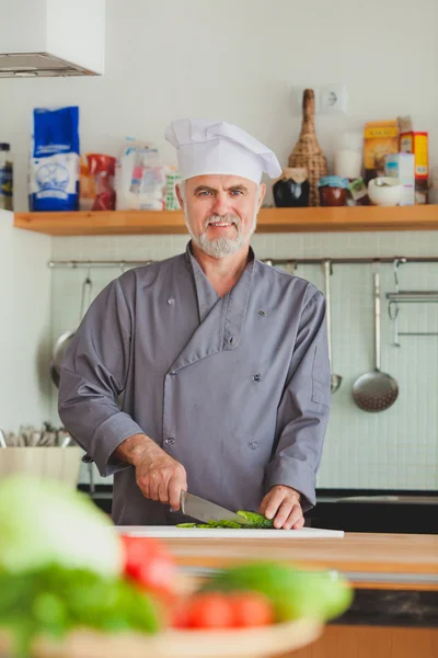 Chef amistoso preparando verduras en su cocina — Foto de Stock