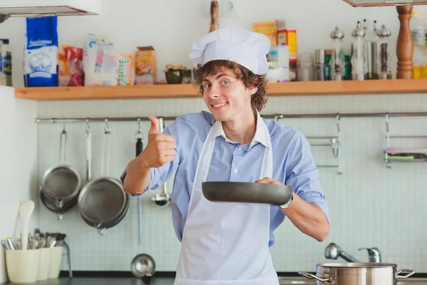 Freundlicher Koch bereitet Essen in seiner Küche zu und zeigt Daumen — Stockfoto