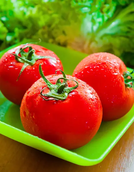 Несколько спелых помидоров на столе в тарелке с салатом — стоковое фото