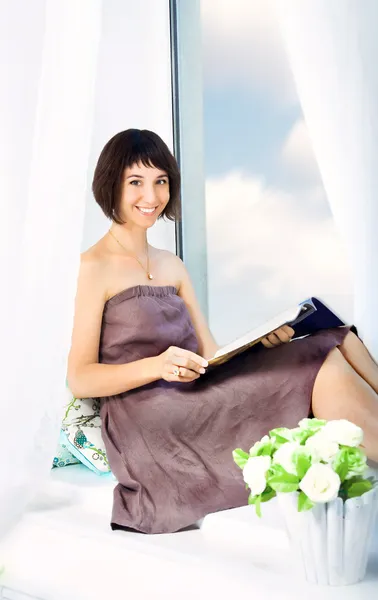 Joven chica sonriente sentada en un alféizar de la ventana en casa — Foto de Stock