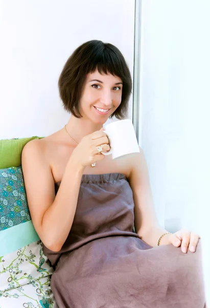Young girl sitting on a window sill and holding a cup — Stock Photo, Image