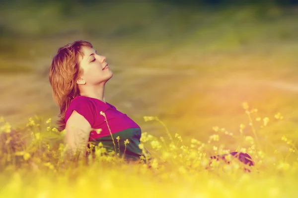 Krásná mladá dívka sedící v trávě při západu slunce a těší se — Stock fotografie