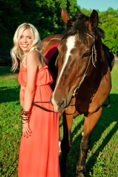 Jovem menina loira atraente sorrindo ao lado de um cavalo — Fotografia de Stock