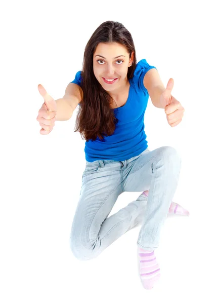Молодая счастливая девушка сидит на полу с большими пальцами вверх — стоковое фото
