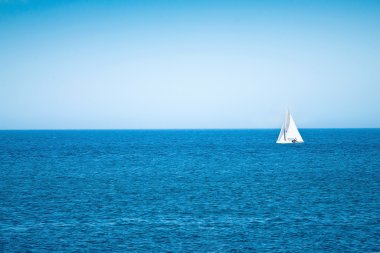 mavi deniz ve ufukta beyaz yelkenli