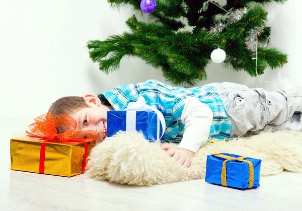 Menino sob a árvore de Natal entre os presentes — Fotografia de Stock