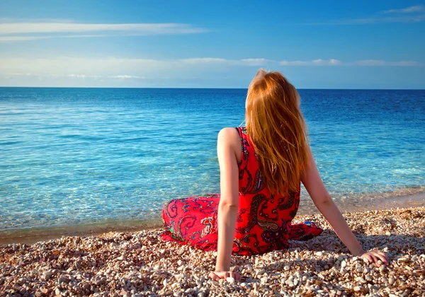 Giovane ragazza seduta sulla spiaggia e guardando il mare — Foto Stock