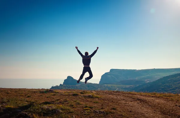 Young man jumping off a cliff with his arms raised — Stock Photo, Image