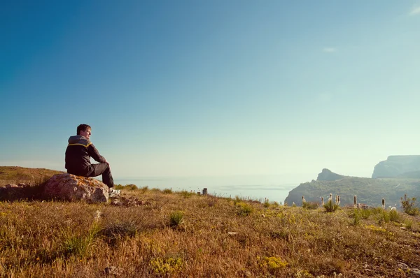 Un giovane uomo siede su una collina e si gode il tramonto — Foto Stock