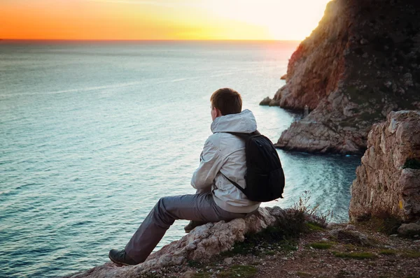 Giovane viaggiatore solitario si siede su una collina e gode di vista sul mare — Foto Stock