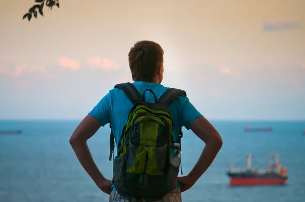 Um jovem com uma mochila viajante olha para o mar — Fotografia de Stock