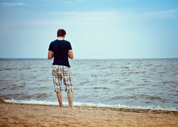 Jovem solitário fica na praia — Fotografia de Stock