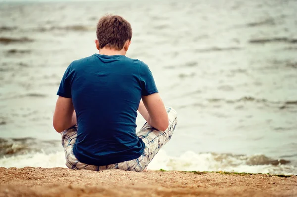 A young man sitting on the beach alone — Stock Photo, Image