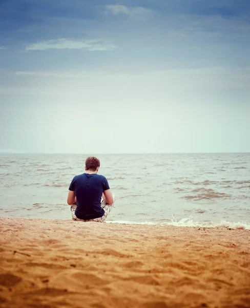 Un joven sentado en la playa solo — Foto de Stock