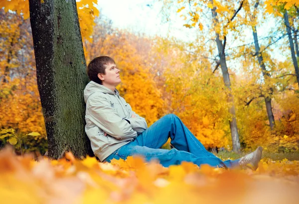 Um jovem sentado ao ar livre em um parque no outono — Fotografia de Stock