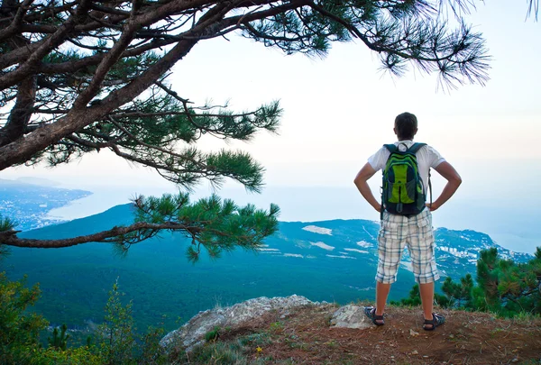 Young tourist with backpack sitting on a hill and looks down — Stock Photo, Image