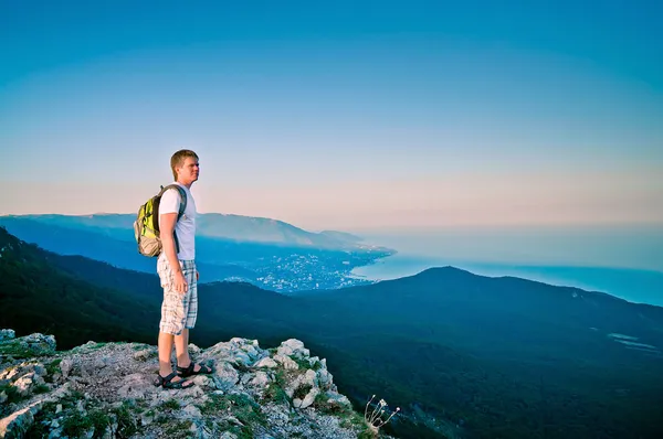Young guy stands up in the mountains at sunset and enjoy the sea — Stock Photo, Image