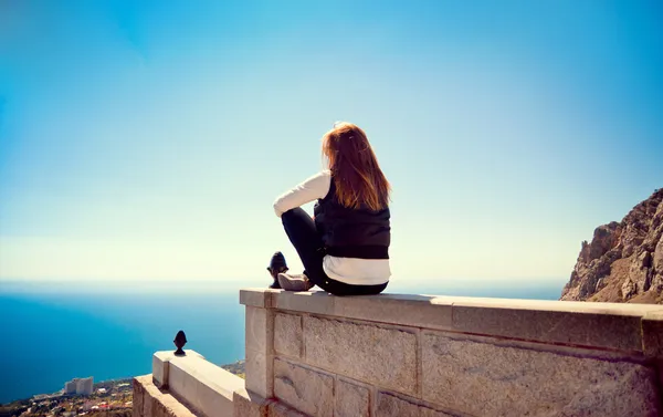 Young girl sitting on a hill looking at the sea — Stock Photo, Image