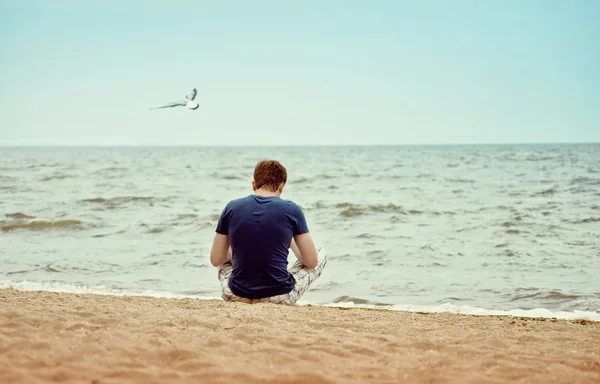 Ένας νεαρός άνδρας κάθεται στην παραλία μόνο 免版税图库图片