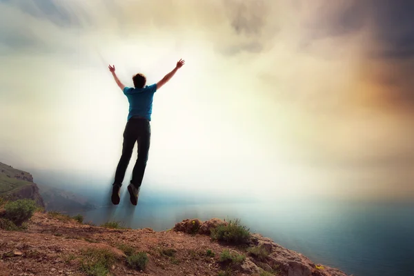 Młody człowiek skacze z klifu z uniesionymi ramionami Zdjęcie Stockowe