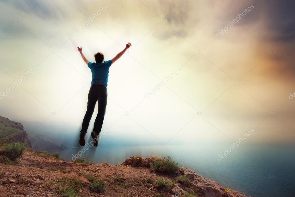 young man jumping off a cliff with his arms raised