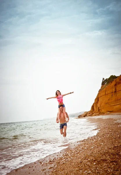 Joven pareja caminando a lo largo de la orilla del mar, chica se sienta en el chico de —  Fotos de Stock