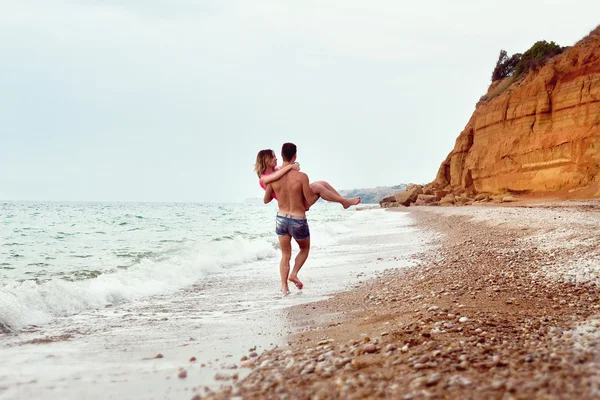 Giovane porta una ragazza sulle mani vicino al mare Fotografia Stock