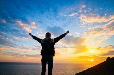 Gün batımında kollarını açmış genç bir adam.