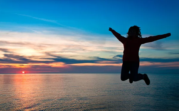 Menina pulando em um fundo de um pôr do sol sobre o mar — Fotografia de Stock