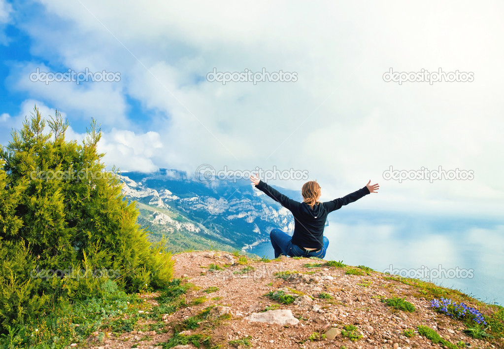 young girl sitting on a hill overlooking the sea and mountains w