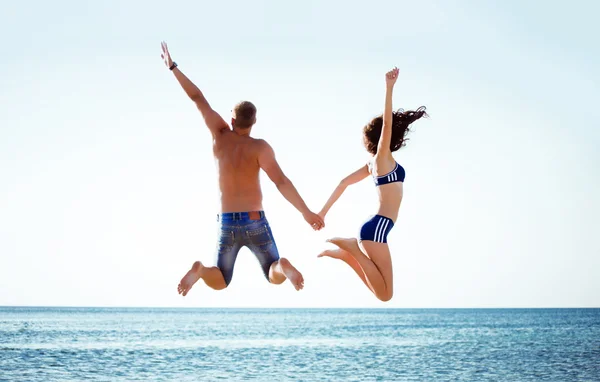 Pretty young couple jumping near the sea — Stock Photo, Image