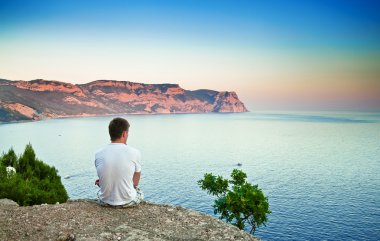genç adam bir tepede oturan ve denizin üzerinde seyir