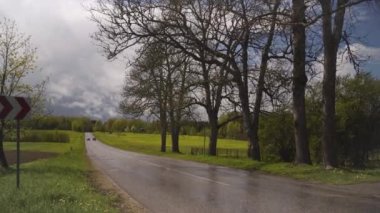 Yağmurdan sırılsıklam olmuş bir yol kıvrımında oklarla yol tabelası. Yağmur ve güneş bahar için tipik havadır. Kırsal kesimde. Letonya