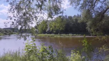 Walk by the river Gauja on a sunny day. Boats sailing with people can be seen behind green leaves. Gauja National Park. Latvia