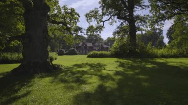 Walk in the old park on a summer day. Old trees in a green park on a sunny day. Old wooden house with columns in the background. Wooden swing on ropes. Ungurmuiza. Latvia