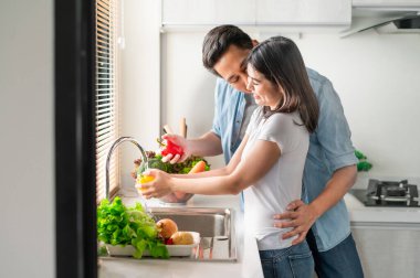 Mutfakta sebze yıkarken gülümseyen mutlu Asyalı çift. Adam kadını yanağından öpüyor.