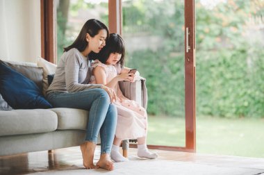 Mutlu Asyalı aile annesi ve kızı evde akıllı telefon kullanıyor..