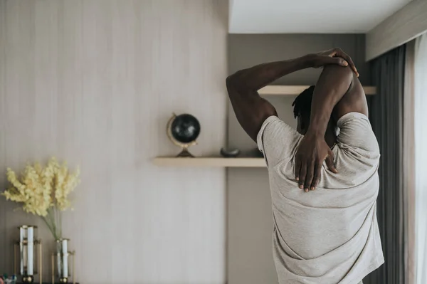 back view of Black Man doing shoulder stretching exercise at home. workout at home