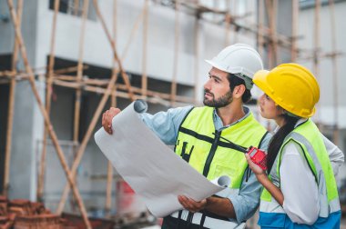 Mimarlar ve mühendisler inşaat sahasının planlarını kontrol etmek için açık havada gayrimenkul projesini denetliyor ve çalışıyor.