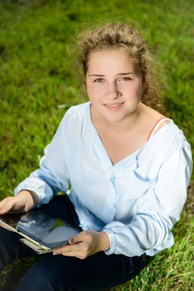 Beautiful young girl using tablet pc and sitting on the green grass — Stock Photo, Image