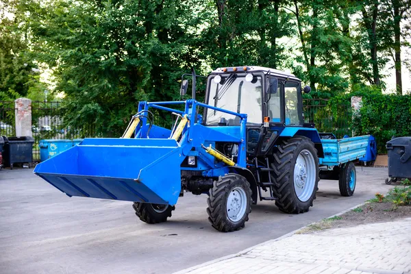 Niebieski ciągnik z przyczepą do czyszczenia terytorium parku w mieście — Zdjęcie stockowe