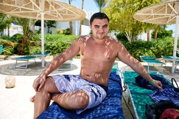 Junger Mann sitzt auf der Sonnenliege am Strand im tropischen Hotel — Stockfoto