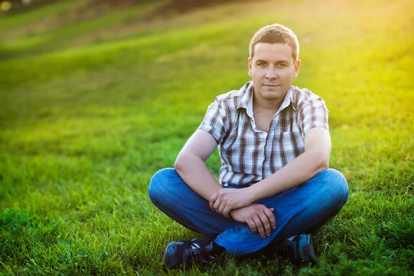 Hadsome man sitting on the green grass in the park — Stock Photo, Image