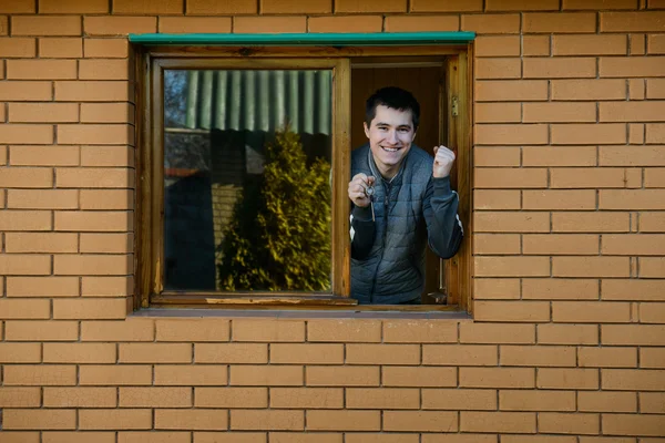 Gelukkig man toont sleutels vanuit het raam van zijn nieuwe huis — Stockfoto