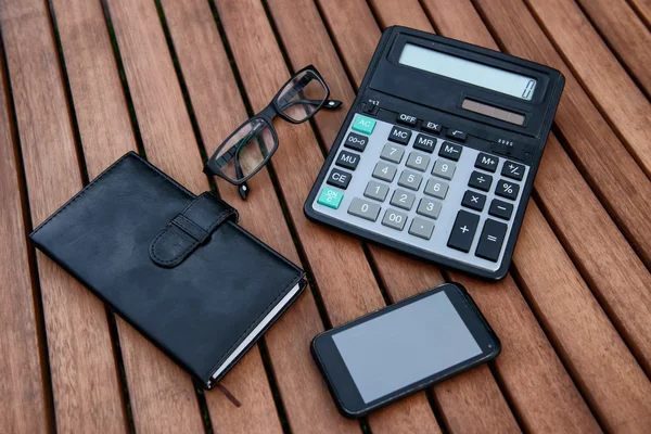 Mobile phone, glasses, calculator, notepad on wooden table. Business accessories concept. — Stock Photo, Image