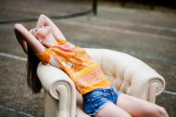 Sensual elegant young woman relaxing on white leather couch outdoors — Stock Photo, Image