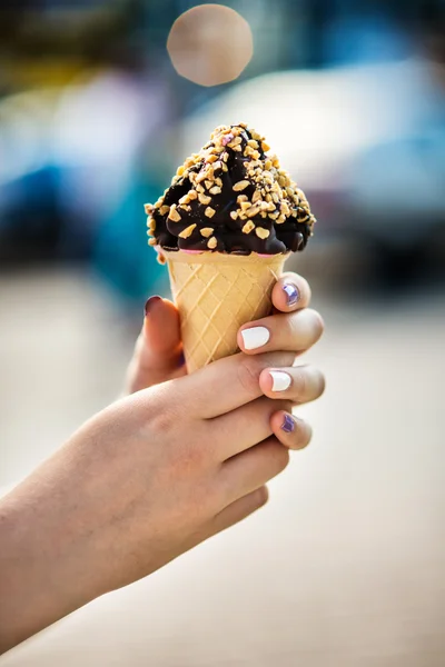 Ice cream cone with nuts and chocolate in hands — Stock Photo, Image