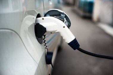Charging an electric car with the power cable supply plugged in clipart