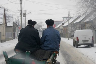 Kışın bir köyde at arabasında oturan iki kişi.